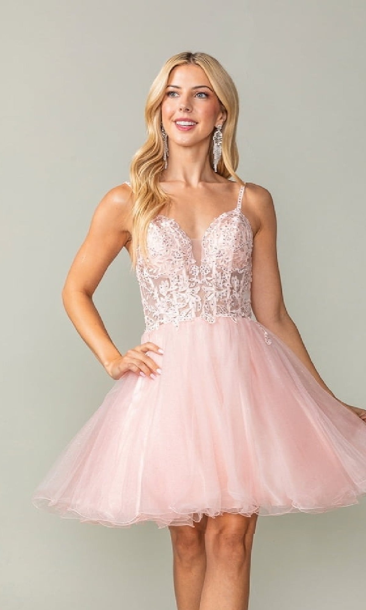 Woman wearing a pink short dress with a lace bodice and tulle a-line skirt against a plain background